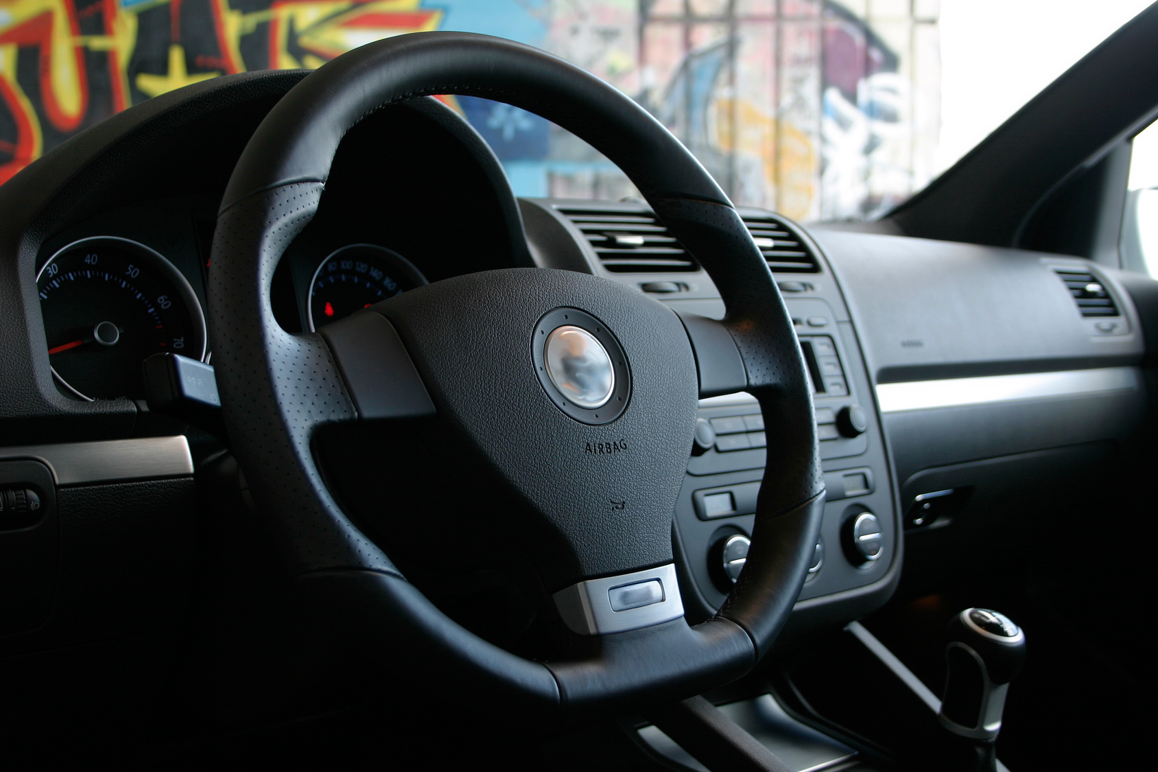 The interior steering wheel of a Volkswagen vehicle. Colorful walls in the background.