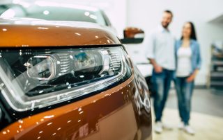 Couple in the background staring at a new orange car