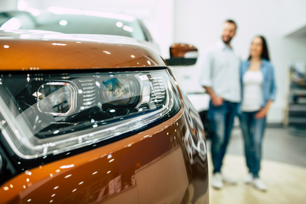 Couple in the background staring at a new orange car