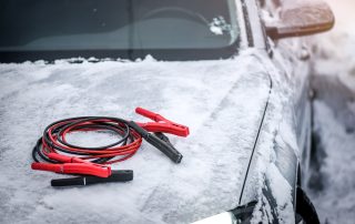 Jumper cables sitting atop a snowy vehicle.