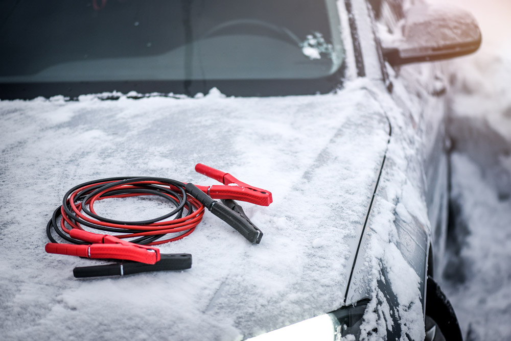 Jumper cables sitting atop a snowy vehicle.