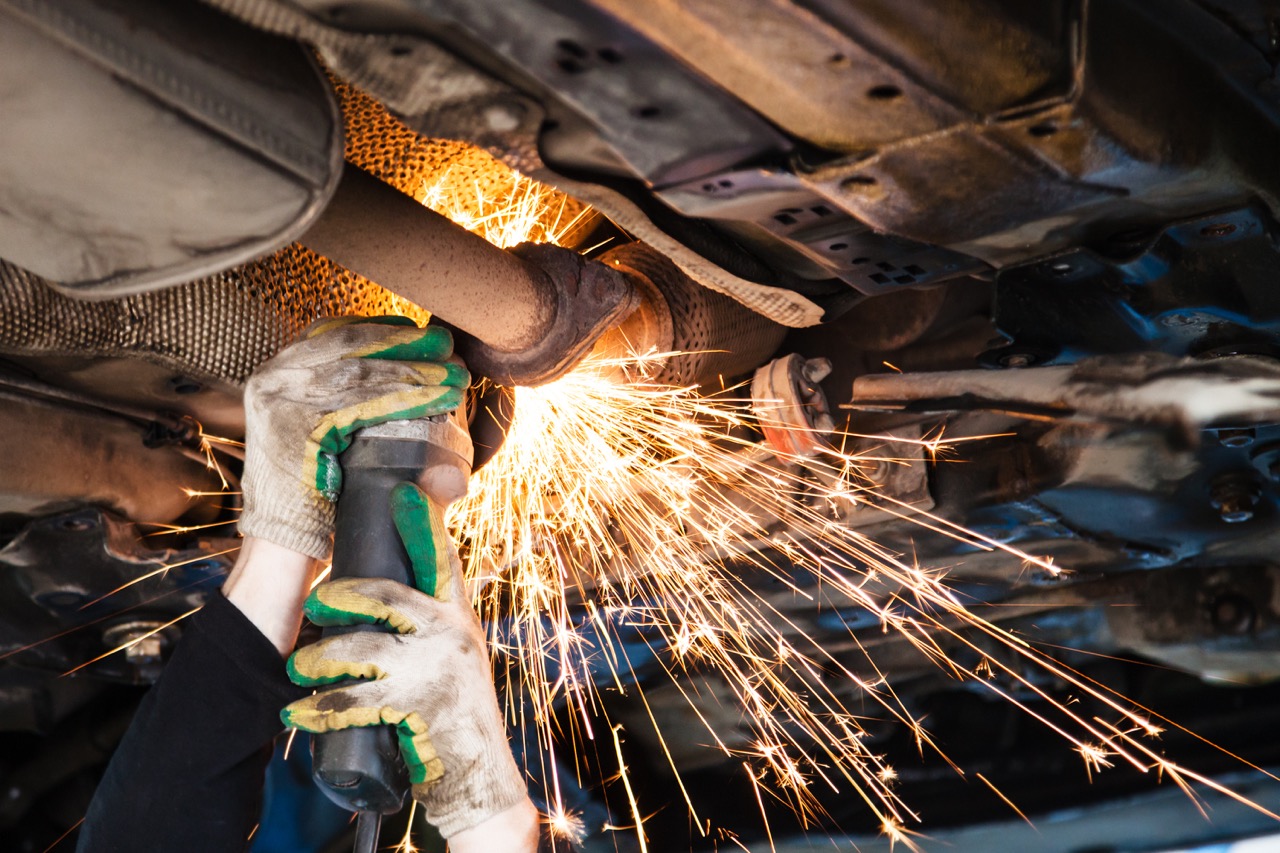 mechanic cuts into muffler on bottom of car