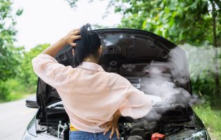 woman looking at her smoking engine on side of road