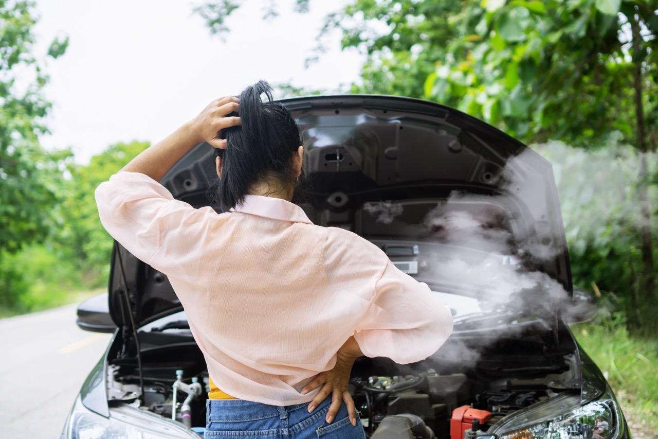woman looking at her smoking engine on side of road